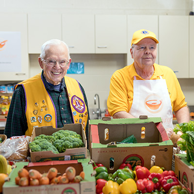 Older men wearing yellow Lions Club vests in front of produce